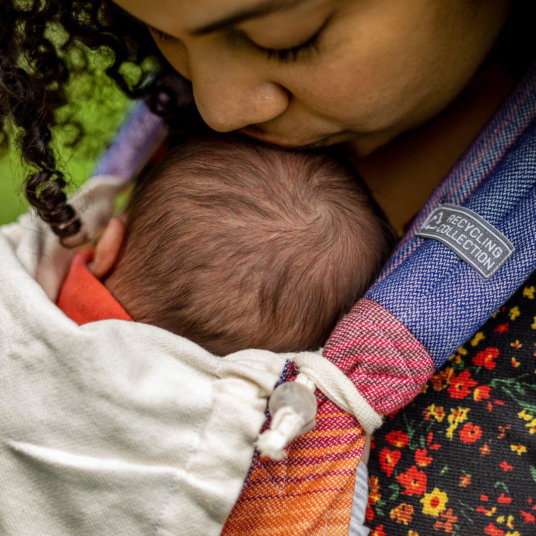 Mutter küsst süßes Baby auf den Kopf in Babytrage Mysol Rainbow Dreamer. 